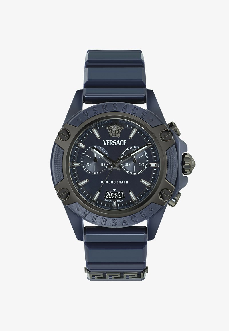 Versace hronogrāfa pulkstenis ar tumši zilu silikona siksniņu, lielu apaļu korpusu, matētām melnām akcentiem, diviem apakšdatiem un iegravētu logotipu uz rāmja.