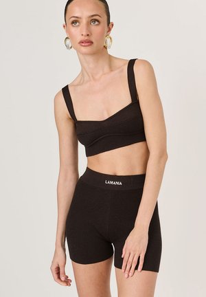 Čierny rebrovaný pletený crop top so širokými ramienkami a zodpovedajúcimi šortkami s vysokým pásom, s logom na páse. Hladká textúra, priliehavý strih.