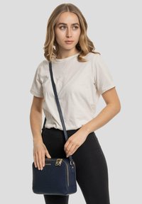 Borsa a tracolla in pelle blu navy con superficie texturizzata, chiusura con zip, dettagli in hardware dorato e tracolla regolabile. Forma rettangolare compatta.