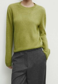 Pull vert clair en maille avec un col rond et des manches longues, associé à un pantalon gris ajusté. Texture douce, design minimaliste.