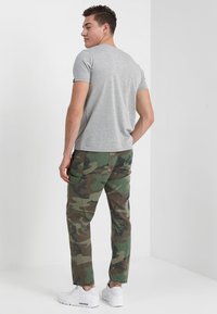 Grå bomulds t-shirt kombineret med grønne camouflagemønstrede bukser, der har en løs pasform, sidelommer og hvide sneakers. Minimalistisk design.