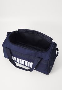 Sac de sport marine en tissu robuste, avec un grand logo blanc, des poignées doubles et une ouverture zippée spacieuse. L'intérieur est simple et sans marquage.