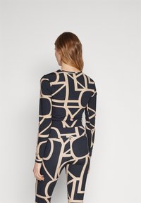 Langermet topp og leggingssett i svart med et beige abstrakt mønster. Laget av stretchy stoff, med en tettsittende design og glatt tekstur.