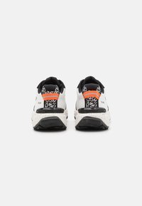 Zapatillas deportivas blancas y negras con una parte trasera texturizada, acentos naranjas y una entresuela moteada. Patrón triangular en el talón.
