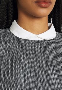 Svart och vit stickad topp med en texturerad tyg, med en vit Peter Pan-krage och subtila veck vid halsringningen.