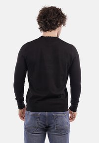 Maglione nero lavorato a maglia con scollatura rotonda e maniche lunghe, dal taglio aderente. Indossato con jeans in denim blu.
