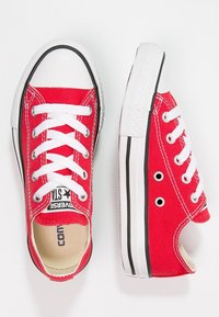 Sneakers in tela rossa con lacci bianchi e punta in gomma. Striscia nera lungo la suola. Presentano fori su ciascun lato per la ventilazione.