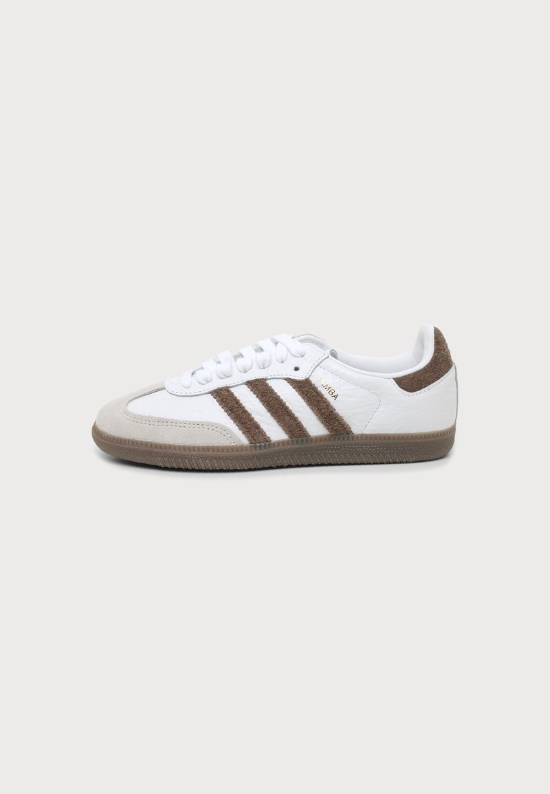 Λευκό και καφέ αθλητικό παπούτσι Adidas Samba με τρεις καφέ ρίγες, κορδόνια και υφή στη σόλα, εμφανιζόμενο από το πλάι σε απλό φόντο.