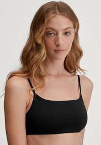 Zwarte naadloze bralette met een vierkante halslijn, dunne verstelbare banden en een gladde textuur. Geschikt om onder kleding te dragen.