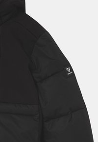 Schwarze Daunenjacke mit glattem Stoff am Oberarm und texturiertem, gestepptem unteren Bereich. Mit einem Logo-Patch an der Schulter.