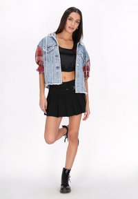 Veste en denim avec ourlet effiloché, manches à carreaux rouges ; crop top noir ; mini jupe plissée noire avec détail de ceinture ; bottines noires à lacets.