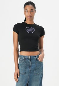 Černé zkrácené tričko s fialovým grafickým potiskem "TOMMY JEANS". Krátké rukávy a přiléhavý střih. V kombinaci s džínsovou sukní.