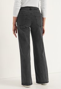 Höga, vida svarta jeans med en slät denimtextur och två bakfickor, med en ren och enkel design.
