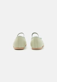 Zapatos de cuero verde claro con una textura suave, forma redondeada y correas en la parte posterior. Presentan una suela beige y un detalle de costura sutil.