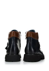 Botas de cuero negro hasta el tobillo con un puño de cuero marrón, que cuentan con una cremallera lateral, superficie texturizada y una suela de goma duradera.