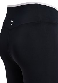 Zwarte hoog getailleerde actieve leggings met een witte elastische tailleband en een klein wit dubbel-chevron logo op de linkerheup.