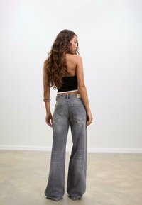 Jeans grigi ampi con un finish sbiadito e due tasche posteriori. Presentati su un modello con capelli lunghi e ondulati, su uno sfondo bianco semplice.