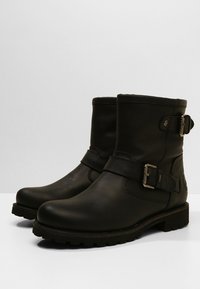 Svarta läderankelboots med rund tå, sidobanddetalj och robust gummisula. Slät yta med minimalt med sömnadsdetaljer.