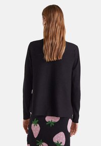 Suéter negro de manga larga con un corte holgado, diseño minimalista y textura acanalada, combinado con una falda negra estampada con fresas rosas.