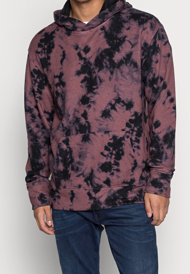 Sudadera tie-dye en color marrón, fabricada con un tejido suave, que cuenta con un bolsillo frontal, mangas largas y capucha con cordón. Con acentos oscuros en todo su diseño.