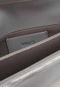 Borsa a mano in nylon grigio con una texture liscia, dotata di una patch con il logo "MNG" e una chiusura con zip argentata nella parte superiore.