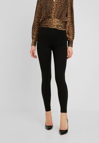Svarta leggings i elastisk väv med hög midja. Matchas med en blus i leopardmönster och svarta högklackade skor.