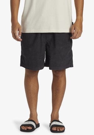 Sorte corduroy shorts med en afslappet pasform, der har en flad front og sidelommer, parret med sorte og hvide slide-sandaler.
