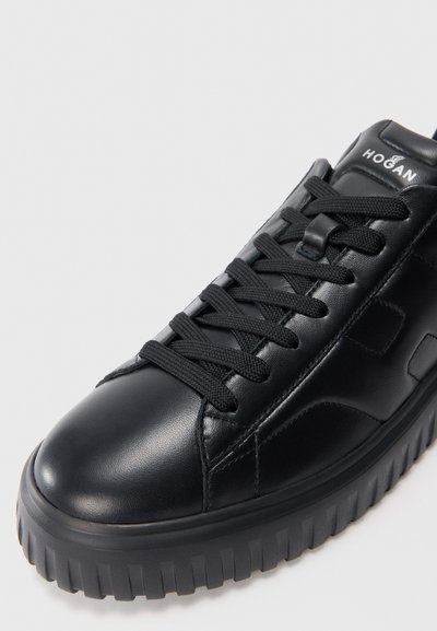 Black leather sneaker with thick ridged sole, black laces, and Hogan logo on padded tongue, photographed on white background.