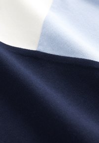 Nahaufnahme eines Stoffes mit drei Farbblöcken: Weiß, Hellblau und Dunkelmarineblau, die Textur und leichte Falten zeigen.