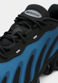 Close-up of a black and blue Nike Air Max sneaker highlighting laces, textured fabric, and logo on the tongue.