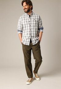 Geruite button-up shirt in grijs en wit, opgerolde mouwen, gecombineerd met olijfgroene broek en bruine sneakers met witte zolen. Casual fit.