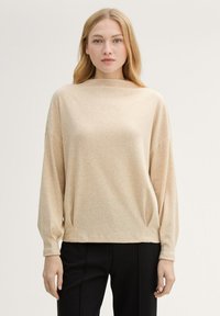 Beżowy sweter z długim rękawem i dekoltem w łódkę, o miękkiej teksturze i luźnym kroju. Posiada opuszczone ramiona oraz delikatne fałdy po bokach.