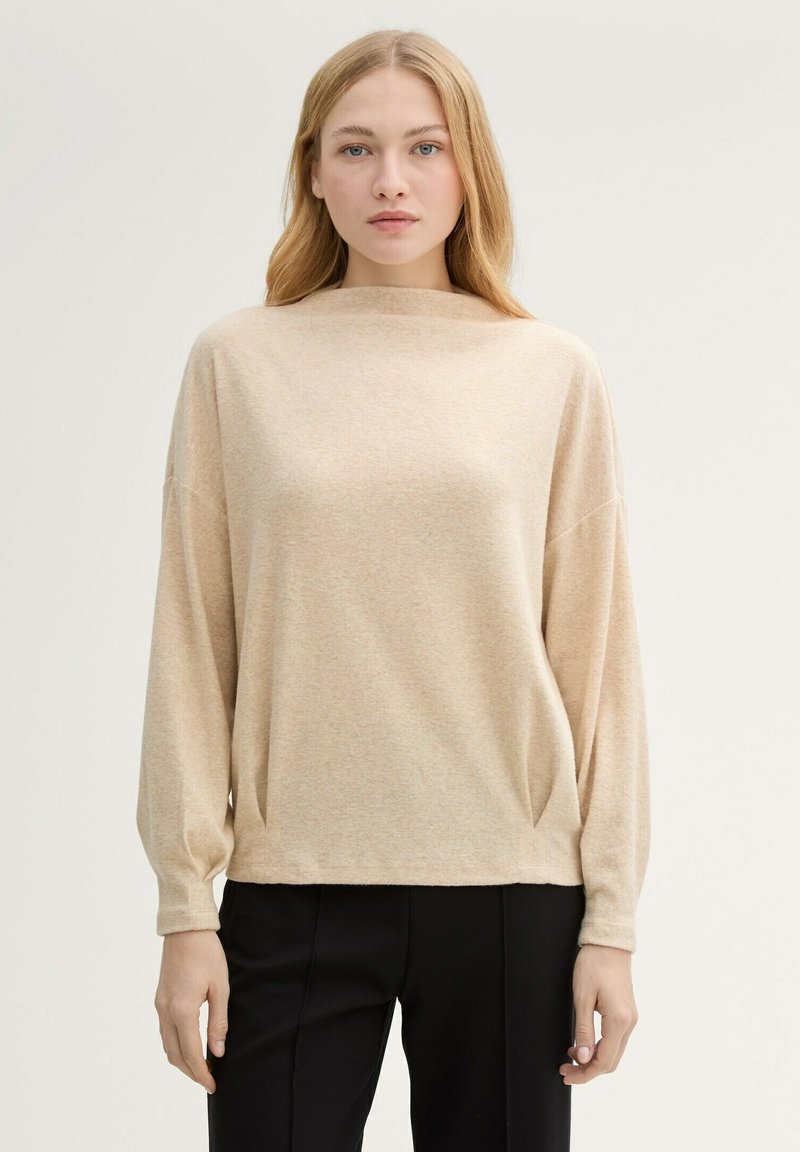 Beżowy sweter z długim rękawem i dekoltem w łódkę, o miękkiej teksturze i luźnym kroju. Posiada opuszczone ramiona oraz delikatne fałdy po bokach.