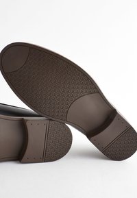 Semelles de chaussures en caoutchouc marron avec un motif de grip texturé, présentant des bords arrondis et des sections lisses, conçues pour la durabilité et l'adhérence.