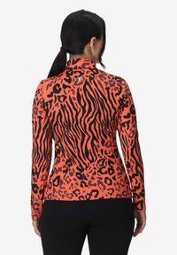 Maglietta a maniche lunghe di un brillante arancione con un motivo a stampa leopardata nera, caratterizzata da un colletto alto e una vestibilità slim. Tessuto testurizzato e elasticizzato.