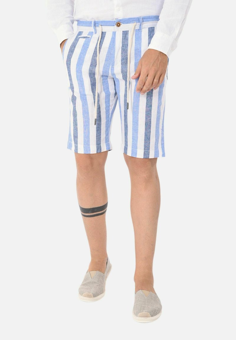 Pantaloni corti in lino a righe blu e bianche con vita regolabile tramite coulisse, due tasche laterali e chiusura con bottone. Abbinati a scarpe grigie slip-on.