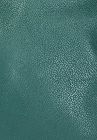 Surface texturé de couleur sarcelle avec un petit motif granuleux typique du matériau cuir, montrant des reflets de lumière et des plis subtils.