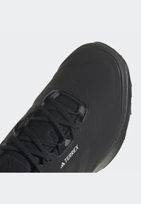 Zapato de senderismo negro con parte superior texturizada, presenta un cierre de cordones en la parte delantera y un prominente logo de TERREX en el costado. Suela de goma para tracción.