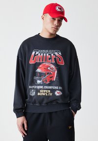 Černá mikina s grafikou "Kansas City Chiefs", logy NFL a ilustrací červené helmy; doplněná červenou kšiltem s logem týmu.