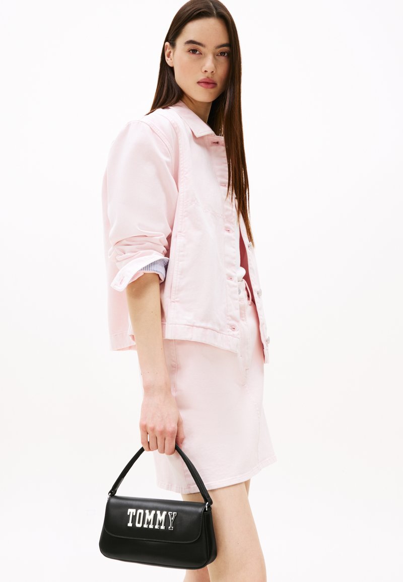 Chaqueta de mezclilla rosa combinada con una falda rosa a juego; bolso negro con logo "TOMMY" en blanco. Textura suave, diseño casual.