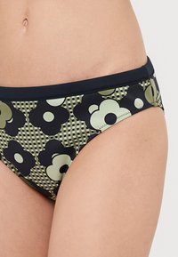 Tengerés bikini alsó sötétkék színben, nagy fekete és világoszöld virágokkal díszített virágmintával, rács háttérrel. Sima textúra, rugalmas derékpánt.