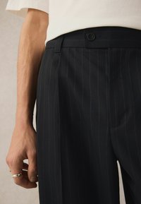 Pantalons bleu marine à rayures avec une coupe ajustée, dotés d'une fermeture par bouton, de poches latérales et d'une texture de tissu lisse.
