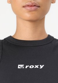 Black ribbed tank top with a round neckline and white "roxy" logo at the center, featuring textured fabric and fitted design.