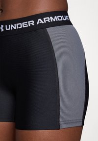 Crne atletske kratke hlače s sivim rebrastim bočnim panelima, s crnim pojasom na kojem je bijeli naziv "UNDER ARMOUR". Glatka tekstura tkanine.