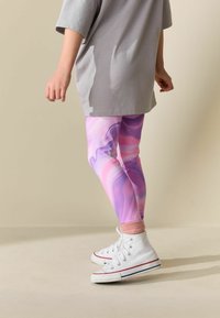 Legginsy w różowo-fioletowy marmurkowy wzór, zestawione z szarą, oversize'ową koszulką i białymi wysokimi trampkami z czerwonymi akcentami.