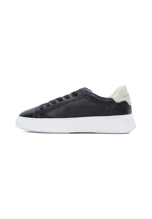 Sneaker bassa in pelle nera con suola bianca spessa e linguetta beige chiaro sul tallone, vista laterale su sfondo bianco.