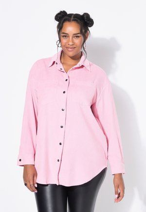 Pink corduroy button-up shirt with two chest pockets, black buttons, and long sleeves, paired with black leggings. Smooth texture.