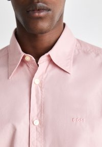 Camicetta rosa chiaro con bottoni, realizzata in tessuto morbido. Presenta un colletto a punta, una leggera trama e il logo ricamato "BOSS" nello stesso colore.