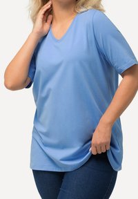 Ljusblå, kortärmad V-ringad t-shirt gjord av mjukt tyg med lös passform och sidslitsar för lätt rörelse, i kombination med mörka jeans.