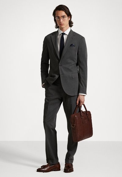 Grijs op maat gemaakt pak met een slim fit, wit shirt, marineblauwe stropdas en pochet. Donkerbruin leren aktetas en schoenen maken de look compleet.
